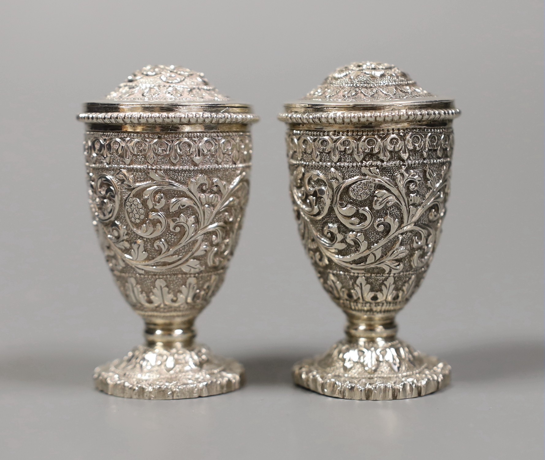 A pair of early 20th century Indian embossed white metal pedestal pepperettes, 7cm, 112 grams, in Elkington & Co, Calcutta, fitted box.